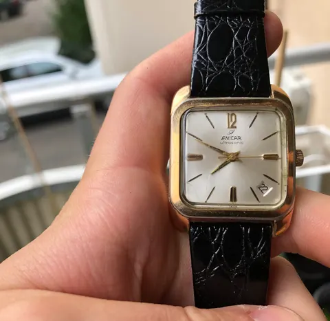 Gold-plated Enicar Ultrasonic with a square case, silver dial, gold baton markers and a date window, held in a hand